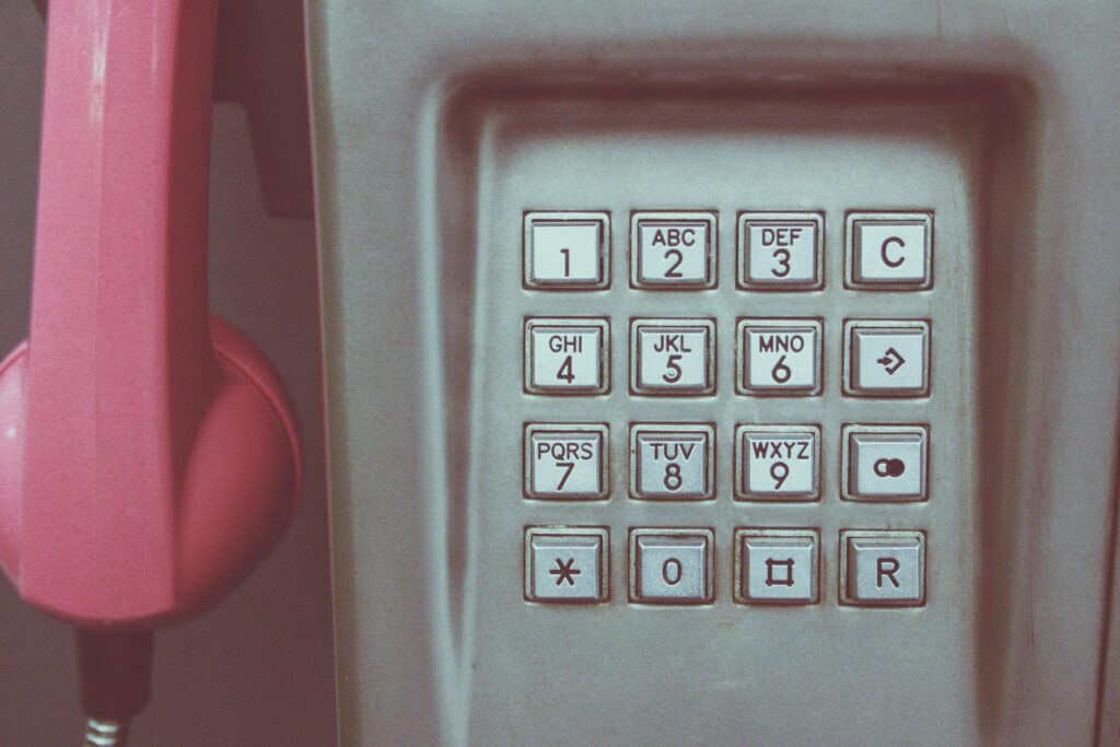 Close-up of a vintage payphone keypad with pink receiver, highlighting retro technology.